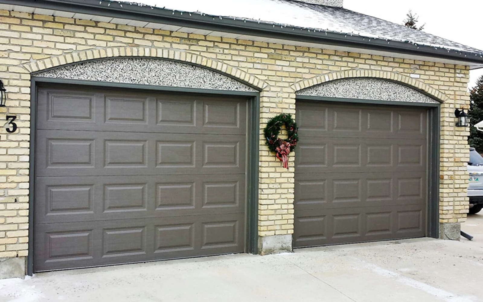 A double garage door repair with dark brown doors with rectangular panels. Set within a yellow brick arch for both garage doors.