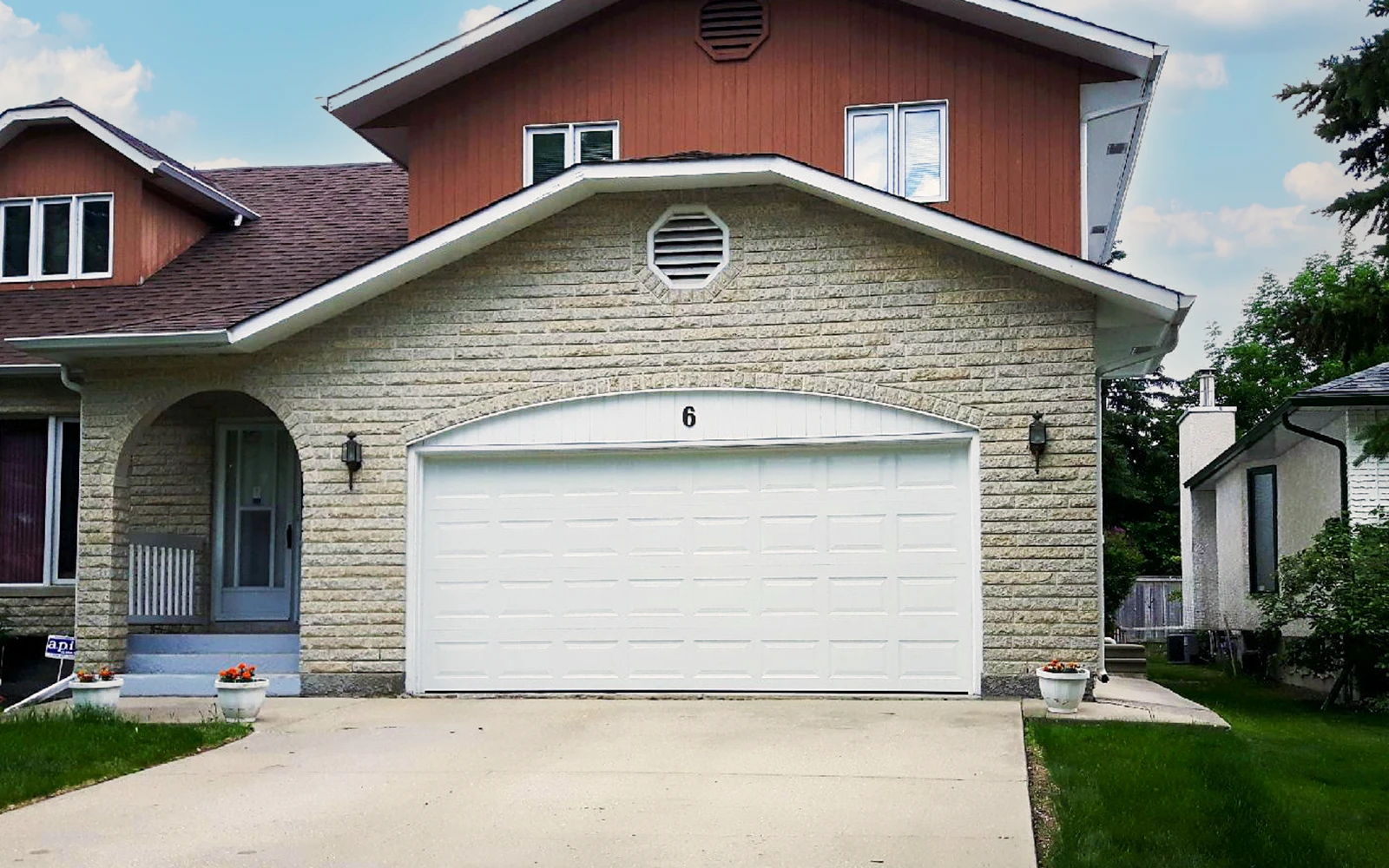 A new white garage door with rectangular panels set in a arched brick frame on a residential home